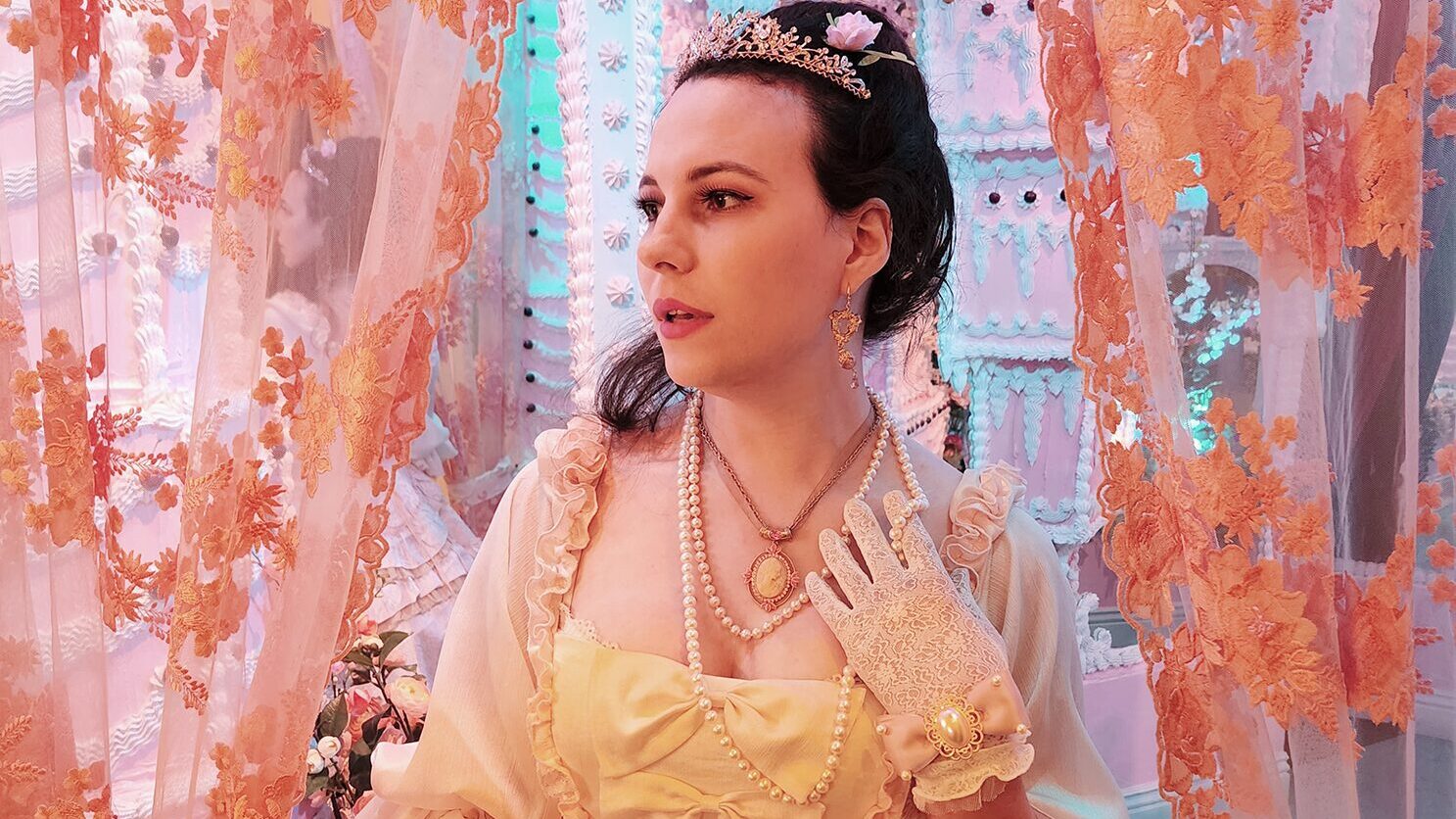 A photo of the author, Nicoletta, pictured in a pink rococo dress with gloves and fan, her dark hair piled high and a tiara on her brow.
